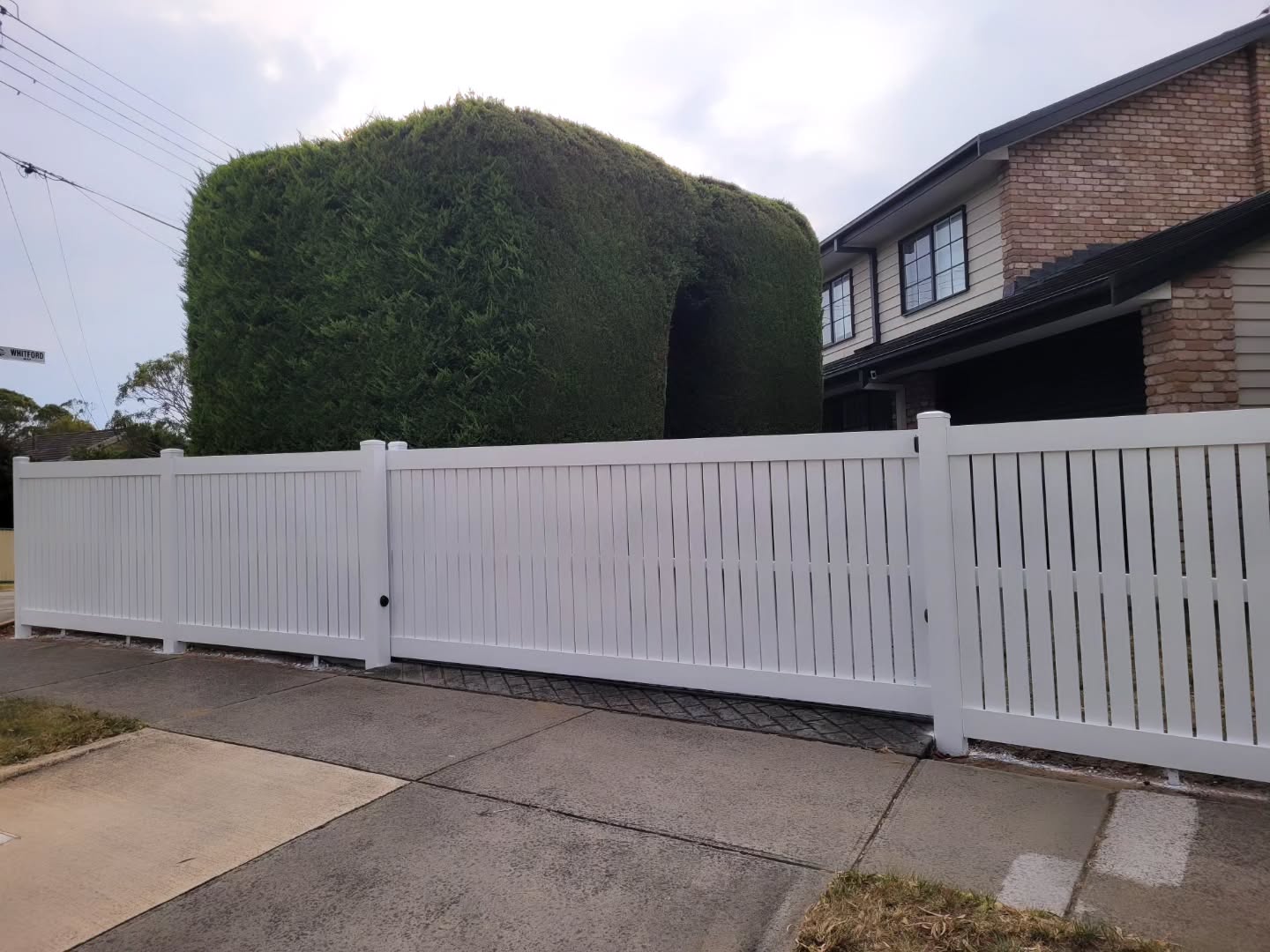 White PVC privacy fence and sliding gate built along a suburban driveway
